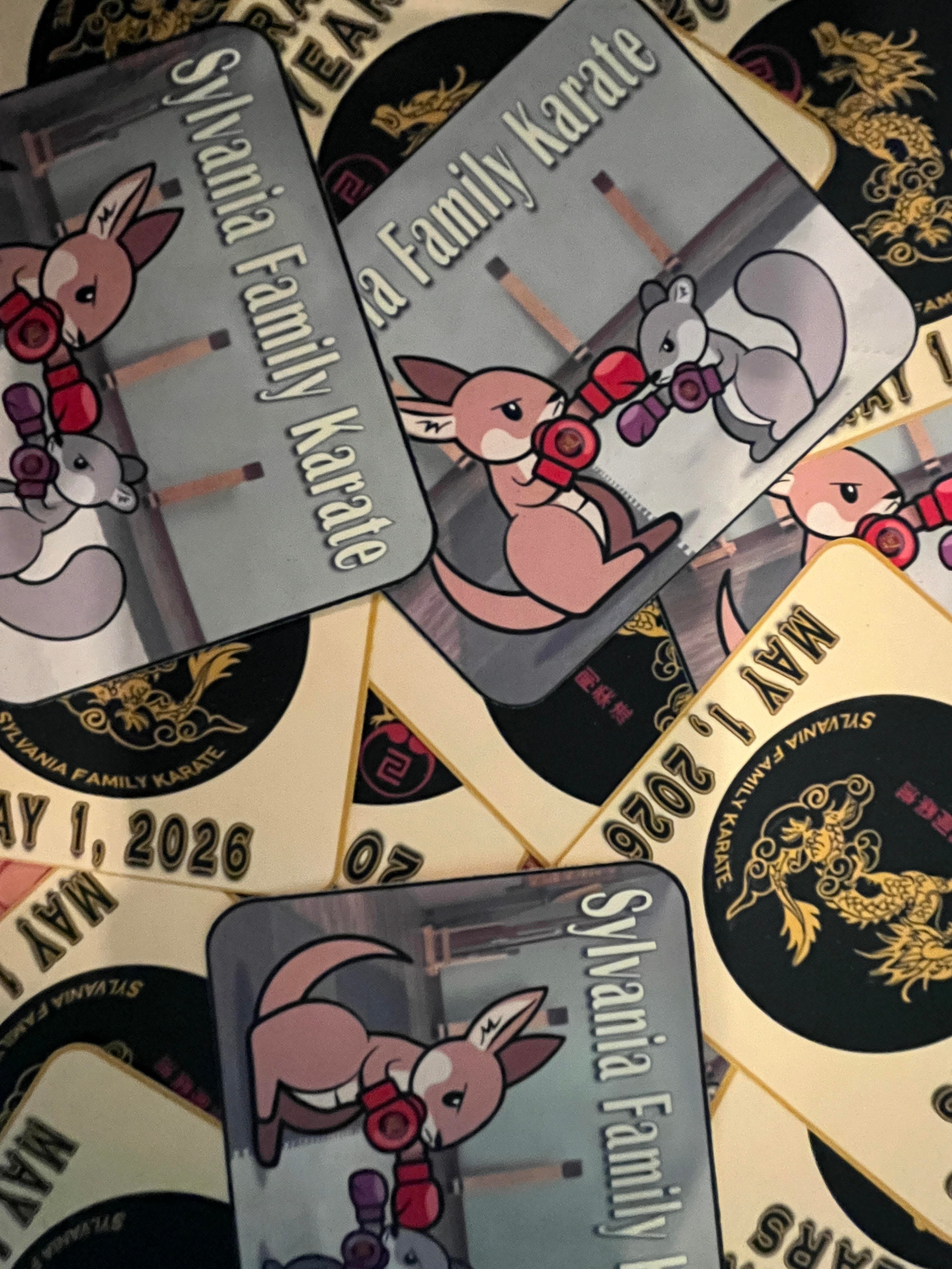 the final printed stickers results; one is a kangaroo and squirrel sparring with 'Sylvania Family Karate' with light yellow text. The second is the SFK logo of a golden dragon on a light golden background with additional text: 'Celebrating 20 Years May 1, 2026'.